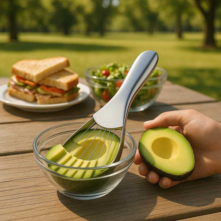avocado Skærer i Rustfrit Stål og Plastik - Hurtig Skæring, 1 stk: A different realistic picnic table setting in a park where the avocado slicer is securely positioned on a portable picnic surface, being showcased alongside an array of picnic food items like sandwiches and salads.