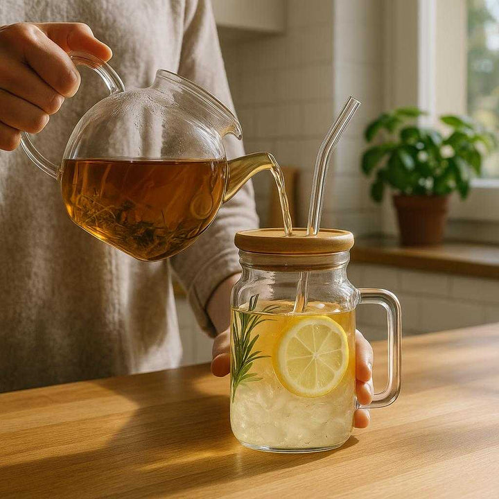 Bambus glaskop med sugerør - Moderne og bæredygtig drikkeglas med hank, låg og sugerør i glas: A realistic kitchen setting where the bamboo glass cup with straw is properly grounded on a wooden countertop, being actively used by a person pouring freshly brewed herbal tea into it.