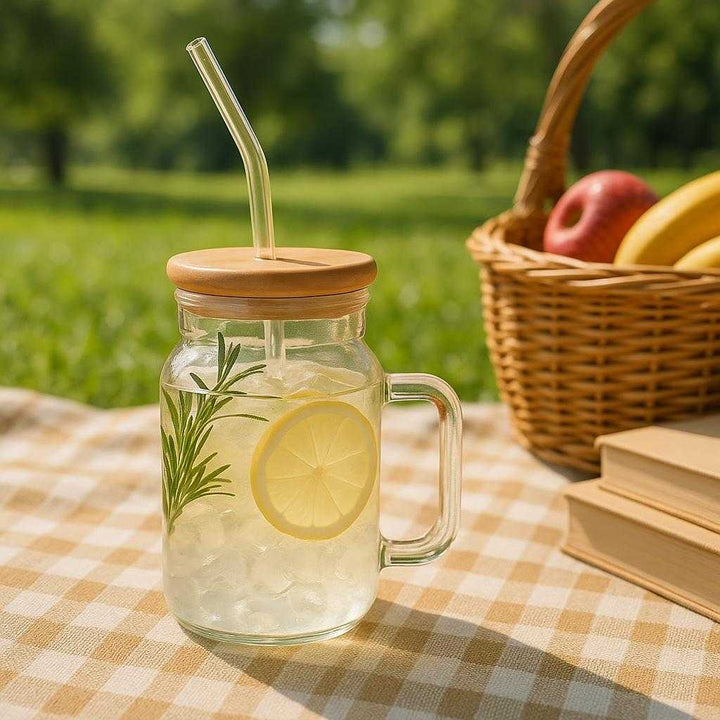 Bambus glaskop med sugerør - Moderne og bæredygtig drikkeglas med hank, låg og sugerør i glas: A different realistic outdoor picnic setting where the bamboo glass cup with straw is securely positioned on a checkered blanket spread out over grass, filled with lemonade and ice.