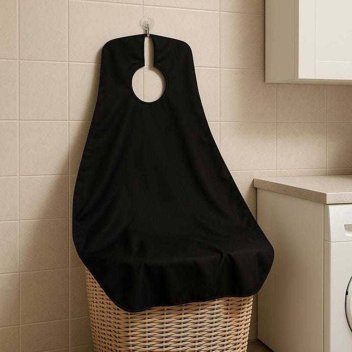 Barberingsforklæde med Sugekopper til Effektiv Hårfangst - Høj Kvalitet og Nem Oprydning: A different realistic home setting in a laundry room, where the barbering cape is neatly hung up on a hook using its suction cups after use.