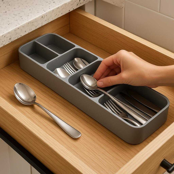 Bestikbakke i justerbar bambus - Optimal organisering af bestik og køkkenredskaber: A realistic kitchen setting where the bamboo adjustable cutlery tray is properly grounded inside a kitchen drawer, being actively used by a hand organizing various cutlery items like spoons, forks, and knives.