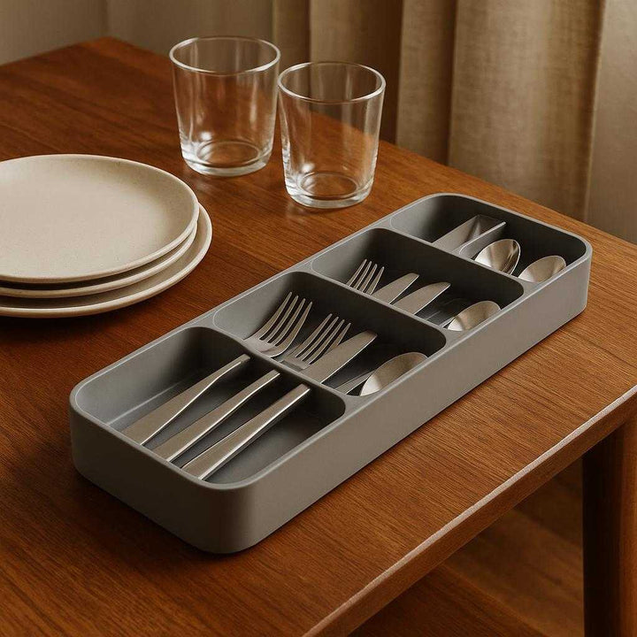 Bestikbakke i justerbar bambus - Optimal organisering af bestik og køkkenredskaber: A different realistic dining table setting where the bamboo adjustable cutlery tray is securely positioned on a wooden table, naturally placed beside a set of clean plates and glasses, ready for a dinner setup.