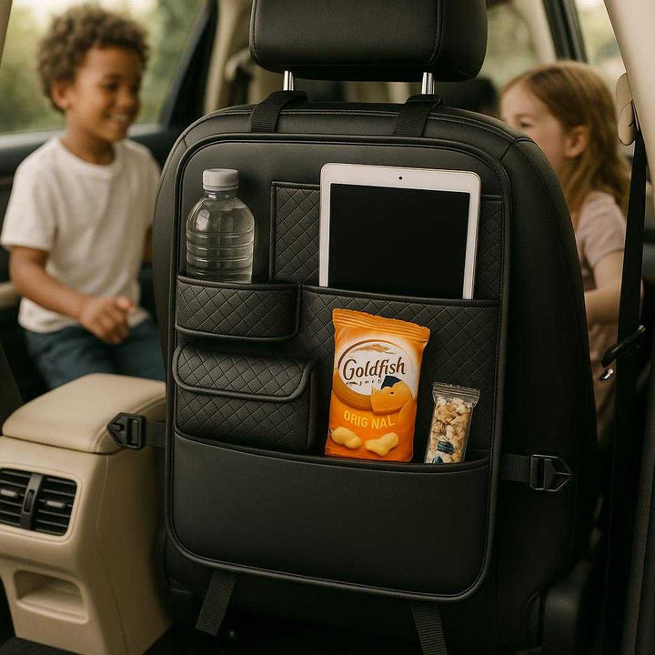 Bilsædeopbevaring i Læderlook med Justerbare Stropper og Flere Rum til Organisering i Bilen. The leather-look car seat organizer is strapped securely to the back of a car seat, filled with travel essentials like water bottles, snacks, and a tablet, in a family vehicle with children playing in the background.