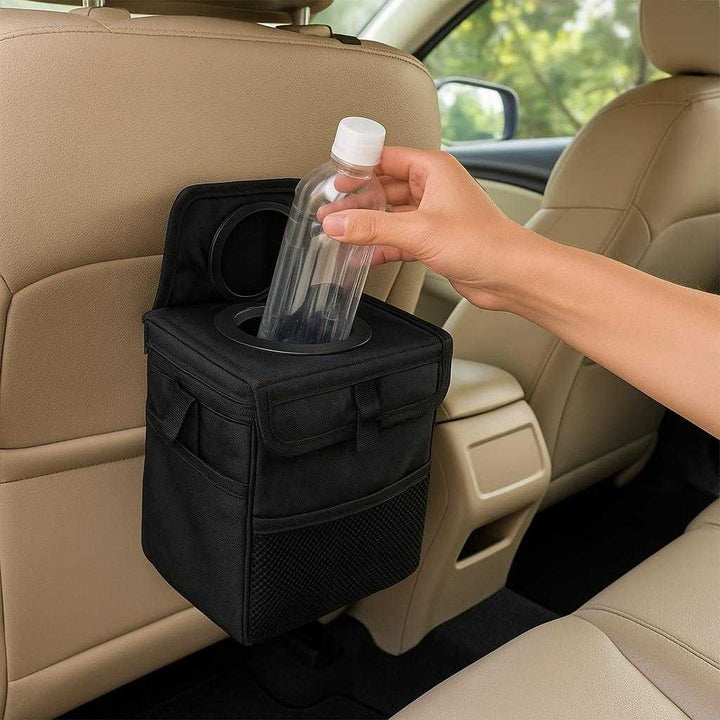 Bilskraldespand i moderne design - Vandtæt og rummelig med nem montering: A realistic car interior setting where the bilskraldespand is properly grounded on the backseat organizer, being actively used by a visible hand placing a plastic bottle inside.