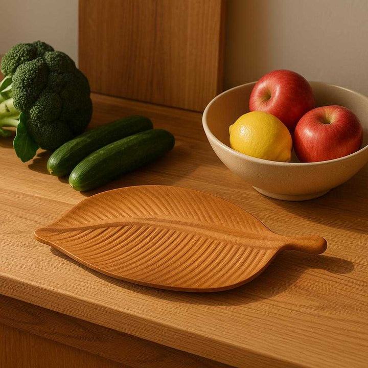 Bladformet fad i naturtræ - Moderne Dekoration til Stue, Badeværelse og Køkken: A realistic kitchen setting where the bladformet fad i naturtræ is properly grounded on a wooden kitchen counter, being naturally placed next to fresh fruits and vegetables, with natural lighting casting realistic shadows and showing clear contact points where the product touches the surface.