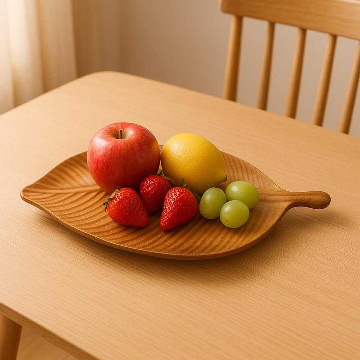 Bladformet træfad i naturtræ - Elegant og Funktionel Dekoration til Moderne Hjem. The elegant leaf-shaped wooden tray is displayed on a minimalist dining table, artfully holding an assortment of colorful fruits, with soft natural lighting enhancing its wooden texture.