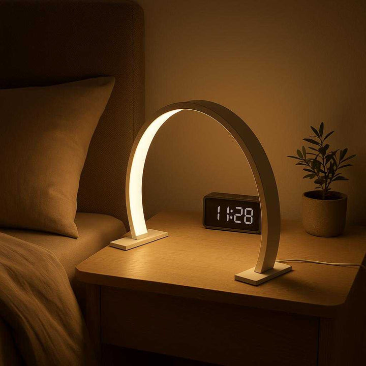 Bordlampe uden ledning – Moon Light LED-lampe med touch, Hvid og Lyserød: A different realistic bedroom setting where the Moon Light LED-lampe is securely positioned on a minimalist nightstand beside a stylish bed setup, being naturally placed to provide ambient lighting near a digital alarm clock and a small plant.