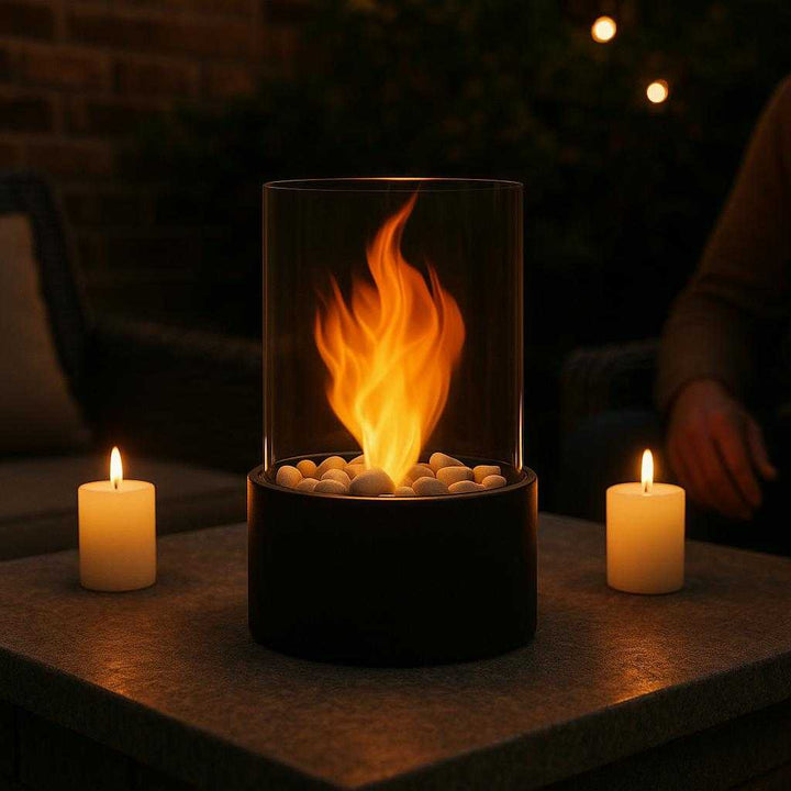Bordpejs i Metal og Glas, Sikker Flammeeffekt, Bærbar - Rektangulær & Cylindrisk: A different realistic outdoor patio setting where the fireplace is securely positioned on a stone table, being used as a centerpiece during a small gathering, with proper physics, gentle night lighting, shadows, and candles on either side, integrating naturally into the cozy environment.