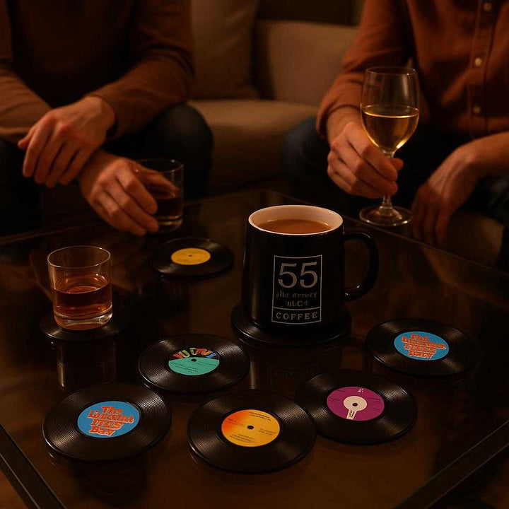 Bordskåner i vinyl-design: Retroinspireret, varmebeskyttende og dekorativ - Sæt med 6 stk: A different realistic living room setting during an evening gathering, where the vinyl-design coasters are securely positioned on a glass coffee table surrounded by friends enjoying drinks.