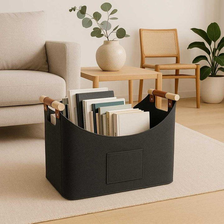 Brændekurv i Filtdesign - Eksklusiv og Robust Opbevaring i Mørkegrå med Læderdetaljer til Moderne Hjem. The dark gray felt basket with leather details is elegantly positioned in a minimalistic living room, storing books and magazines, complementing contemporary furniture and decor.