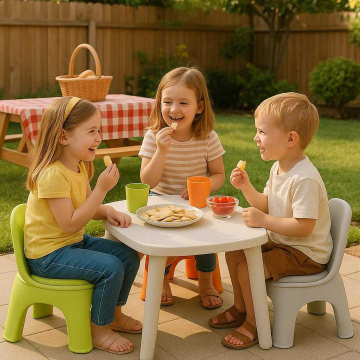 Børnestol i Grøn, Orange og Lysegrå - Stilfuld og Holdbar Plastik Stol til Børn. A sunny backyard setting where the green, orange, and light gray children's chair sits on the patio, perfectly integrated into a family picnic scene with kids enjoying snacks around a small table.