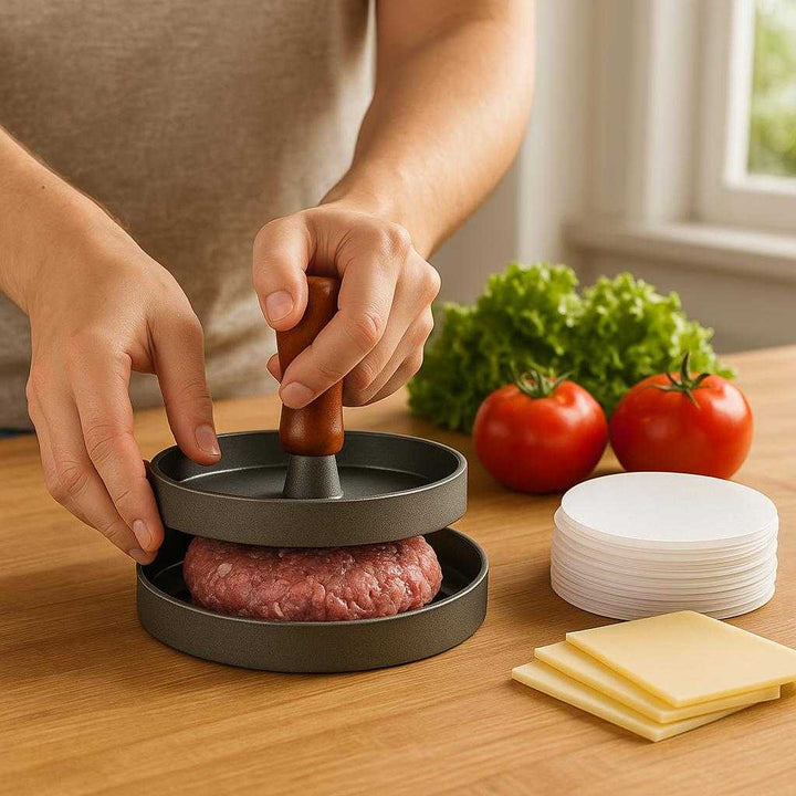 Burgerpresser i aluminium og træ - Skab perfekte, ensartede burgere hver gang: A realistic kitchen setting where the burger press is properly grounded on a wooden countertop, being actively used by a person's hands to flatten a ball of burger meat, surrounded by ingredients like lettuce, tomatoes, and cheese.