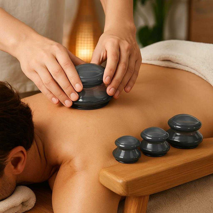 Cupping sæt i silikone - Forbedrer blodcirkulationen og lindrer muskelspændinger: A realistic spa setting where the silicone cupping set is properly grounded on a wooden massage table, being actively used by a massage therapist on a person's back.