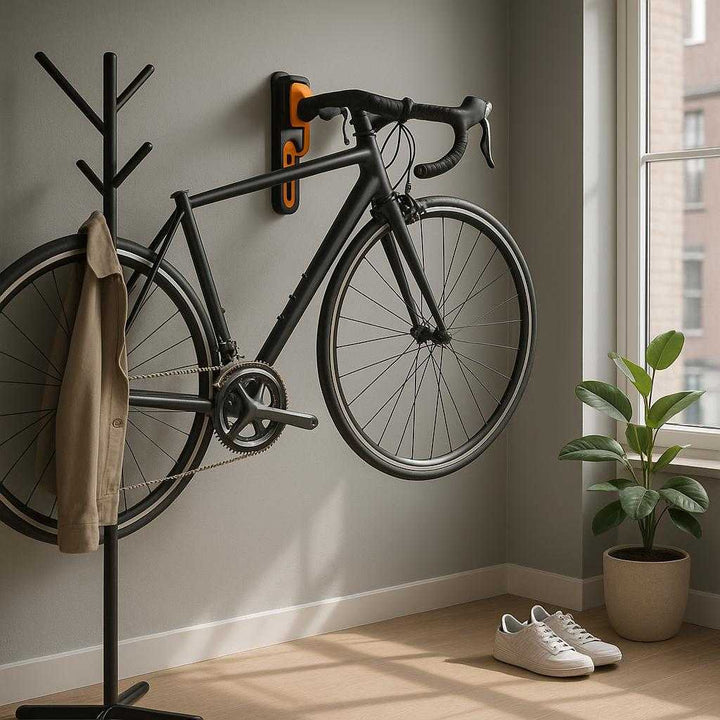 Cykelholder til væg - Justerbar og pladsbesparende løsning i fire farver. A modern urban apartment entryway, where the bike holder is securely mounted on a soft gray wall next to a stylish coat rack. A sleek road bike is effortlessly hung on the holder, showcasing its sturdy support and space-saving design. Natural light floods through a large window, casting gentle shadows on the floor. Nearby, a potted plant and a pair of sneakers add a touch of warmth and livability to the scene.