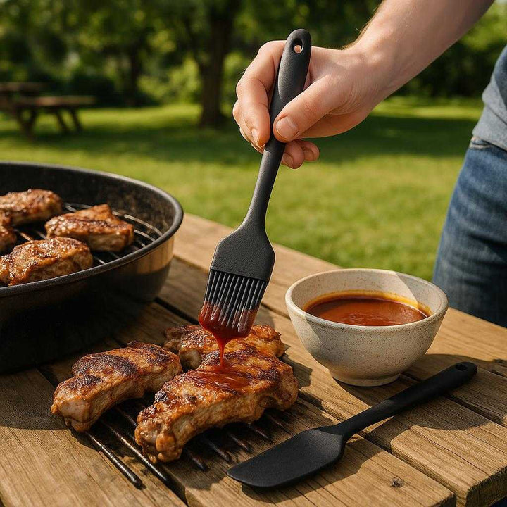 Dejskrabere Sæt i Silikone – Høj Kvalitet, 6 Varmeresistente Redskaber i Rød og Sort: A different realistic outdoor barbecue setting where the silicone brush is securely positioned on a wooden picnic table, being used to apply sauce on grilled meat.