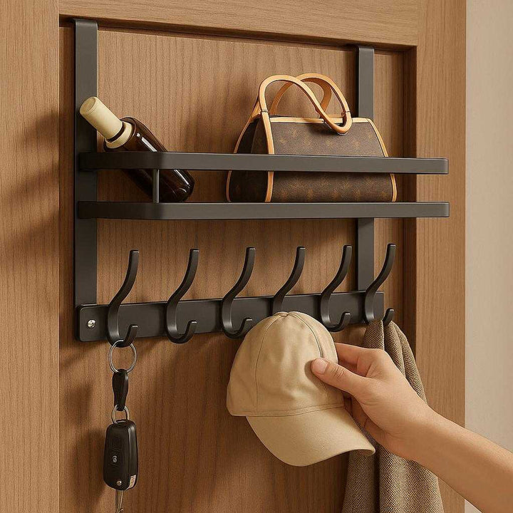 Dørehængt knagerække i metal – Pladsbesparende og multifunktionel opbevaringsløsning i grå: A realistic entryway setting where the product is properly grounded on the back of a wooden door, being actively used to hold multiple items like keys, a scarf, and a hat, with a purse placed on the shelf above.