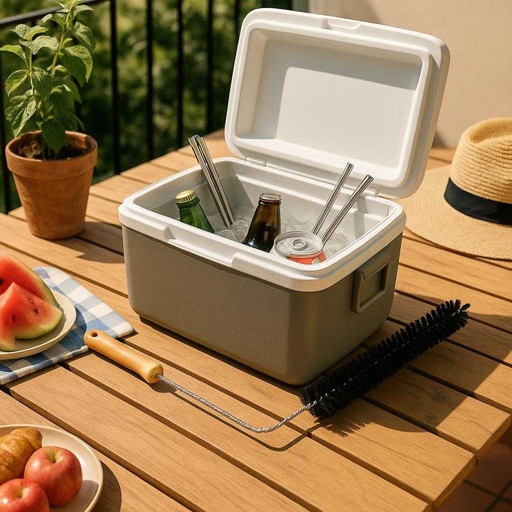 Flaskebørste i træ og metal - Perfekt til rengøring af smalle rum og flasker. An outdoor picnic scene on a sunlit terrace, where the flask brush is casually placed on a wooden table next to an open cooler filled with assorted drinks and reusable metal straws. The open lid of the cooler suggests cleaning is in progress. A potted plant and a sun hat add ambiance, while the brush's steel and nylon bristles glint subtly in the direct sunlight, emphasizing its durability.