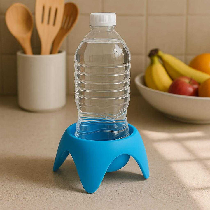 Flaskeholder i Silikone - Praktisk Støtte til Flasker i Blå, Grøn, Lilla og Orange: A realistic kitchen countertop where the silicone bottle holder in blue is properly grounded holding a water bottle steadily, surrounded by various cooking utensils and a fruit bowl, with natural morning light streaming in casting realistic shadows and clear contact points on the counter.