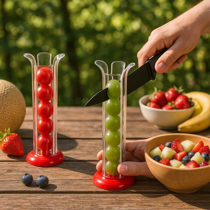 Frugtskærer i Transparent Hvid - Hurtig Skæring og Sikkerhed - Plastik og metal: A different realistic picnic table setting where the product is securely positioned on a wooden table, being used to hold grapes as they are prepared for a fruit salad, surrounded by a colorful array of fresh fruits and a bowl, with proper physics, shadows, and realistic integration into the outdoor environment showing sunlight filtering through tree leaves.