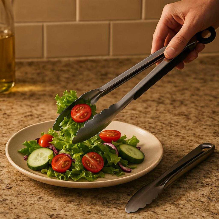 Grilltang i Rustfrit Stål med Låsemekanisme - Professionel og Sikker Madlavning: A different realistic indoor kitchen setting where the stainless steel grill tongs are securely positioned on a countertop beside a ceramic plate with salad, being used to serve fresh vegetables into the plate, under warm kitchen lighting that casts soft shadows and integrates naturally into the cooking environment.