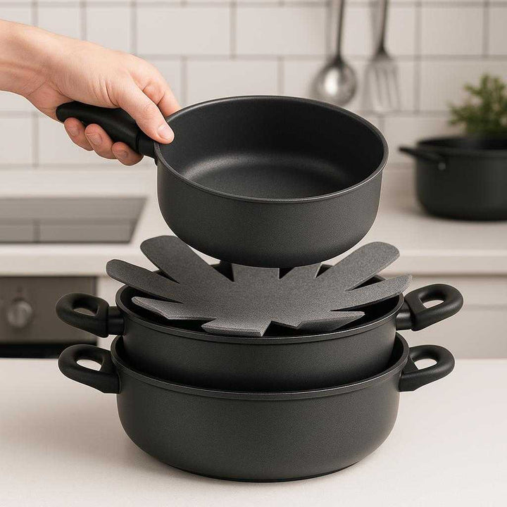 Grydeskåner i Filt - Professionel Beskyttelse til Gryder og Pander med Blomsterformet Design. A set of flower-shaped felt pot protectors neatly stacked between non-stick pots and pans in a sleek, modern kitchen to prevent scratching, while a pot is being lifted from the stack.