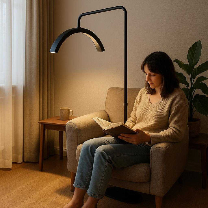 Gulvlampe i Guld, Sort, Hvid og Pink – Elegant Buet Design med LED-belysning: A realistic living room setting where the lamp is properly grounded on a wooden floor, illuminating a cozy reading nook.