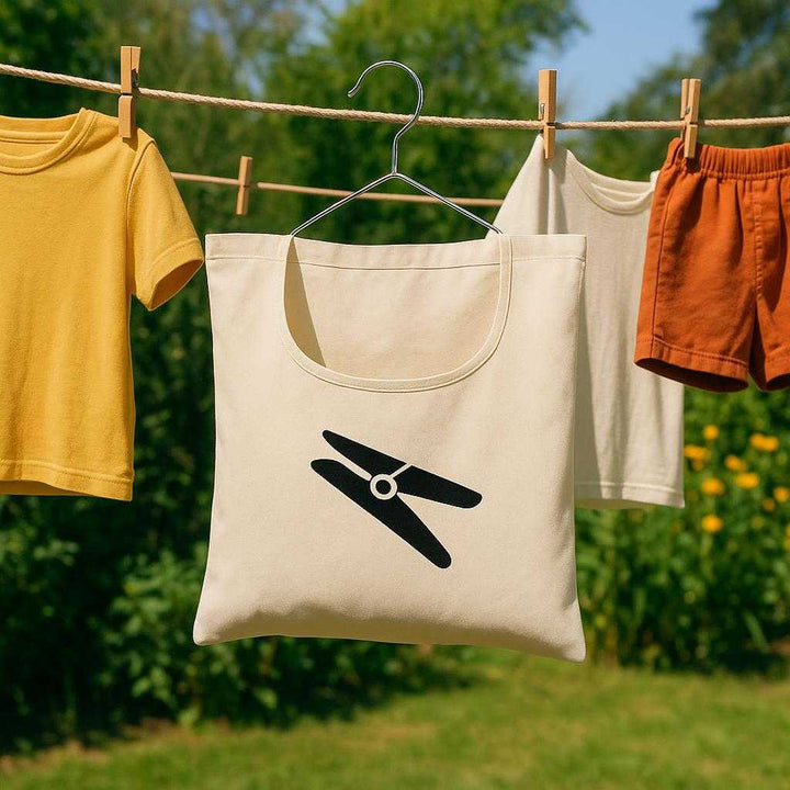 Hanging Storage Taske i Stof og Plastik - Organiserer Tøjklemmer, Let at Hænge Op, 1 stk: An outdoor garden setting with a clothesline where the hanging storage task is securely positioned on the line, naturally placed amidst various colorful clothes drying in the sun.