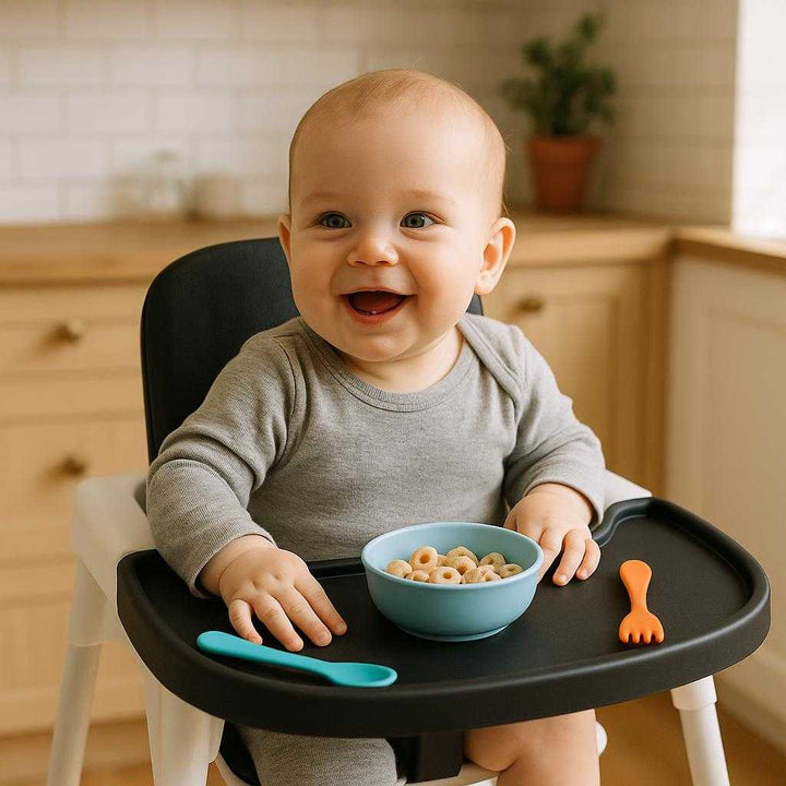 Højstolsbakke i Moderne Design - Praktisk og Stilfuld Spisebakke til Baby Højstol i Sort, Hvid og Grå: A realistic kitchen setting where the product is properly grounded on a highchair, actively being used by a smiling baby sitting in the chair, with natural lighting casting realistic shadows on the tray and clear contact points where the tray attaches to the chair.
