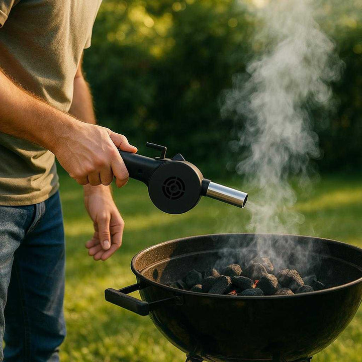 Håndblæser i Kompakt Design – Professionel Sort Håndsving Blæser til Kul og Pejs. The sleek black hand blower is used by a camper to ignite a charcoal barbecue grill in a lush green garden, with smoke rising gently in the afternoon sun.