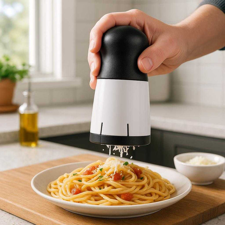 Hånddrevet 3-i-1 Rivejern - Perfekt til Ost, Grøntsager og Nødder i Moderne Sort og Hvid Design: A realistic modern kitchen setting where the Hand-Cranked 3-in-1 Grater is properly grounded on a wooden cutting board, being actively used by a person to grate cheese over a freshly prepared pasta dish.