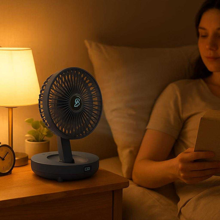 Håndventilator med Batteri - Moderne, Støjsvag og Foldbar Design i Blå og Hvid Farve: A different realistic bedroom setting where the fan is securely positioned on a bedside table, facing the bed and gently blowing towards a person relaxing and reading a book.