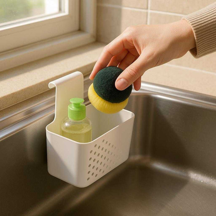 Hængende skabsorganisator – Multifunktionel opbevaring til køkken og bad i moderne hvid plast: A realistic kitchen setting where the product is properly grounded on the edge of a stainless steel sink, being used by a person to hold a dish scrubber and a small bottle of dish soap.