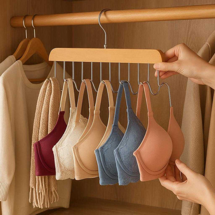 Holder i træ og metal til BH'er og tilbehør - Pladsbesparende og nem organisering: A realistic walk-in closet setting where the holder is properly grounded on a wooden wardrobe rod, being actively used to organize a variety of colorful bras and accessories, with natural lighting casting realistic shadows and showing clear contact points where the product touches the wardrobe.