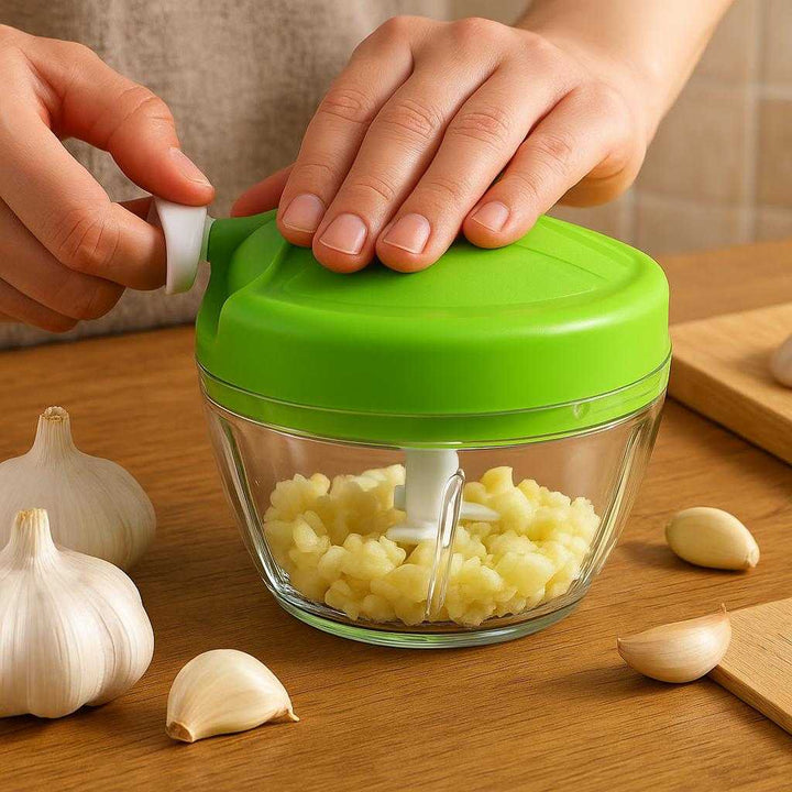 Hvidløgshakker med Drejefunktion i Plast & Rustfrit Stål - Kompakt og Nem at Bruge: A realistic kitchen setting where the garlic chopper is properly grounded on a wooden kitchen counter, being actively used by a person who is holding the handle firmly with one hand and pressing the top to chop garlic cloves visible inside.