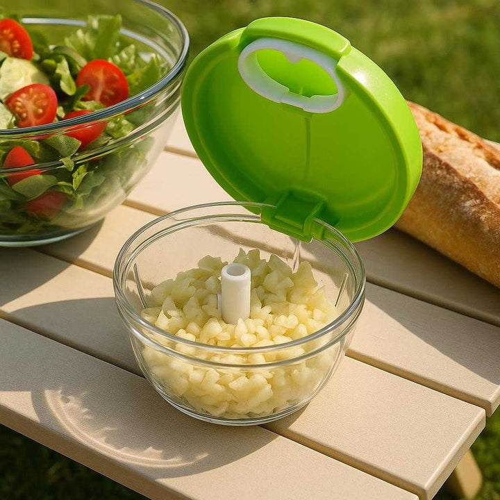 Hvidløgshakker med Drejefunktion i Plast & Rustfrit Stål - Kompakt og Nem at Bruge: A different realistic picnic setting where the garlic chopper is securely positioned on a portable picnic table, naturally placed next to other picnic items like a salad bowl and bread.