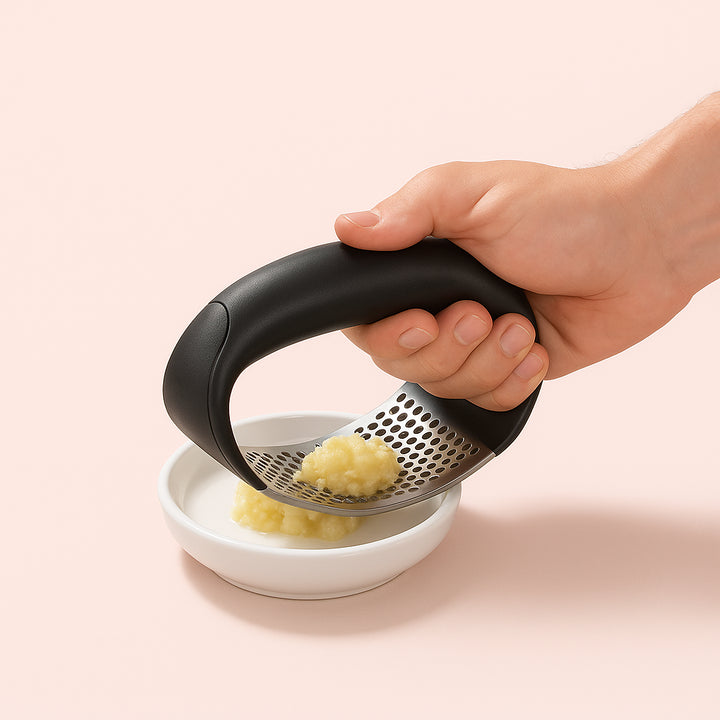 Enhanced Hvidløgspresser i Rustfrit Stål med Ergonomisk Buegreb - Professionel og Moderne Design: An outdoor barbecue area with the product securely positioned on a metal table next to a grill, surrounded by various spices and sauces.