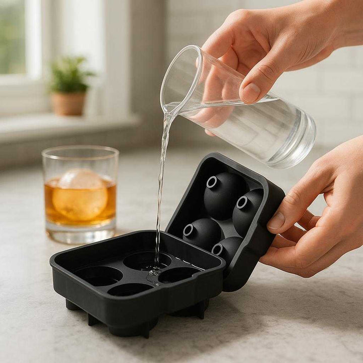 Isboldform i Silikone - Skab Perfekte Runde Isterninger til Whisky, Cocktails og Iskaffe: A realistic kitchen countertop setting where the silicone ice mold is properly grounded on the marble surface, being actively filled with water by a pair of hands.