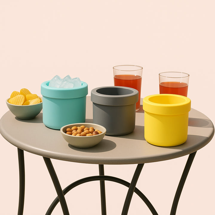 Enhanced Isterningebøtte i Silikone – Praktisk og Kompakt Opbevaring i Blå, Grå og Gul. The compact silicone ice bucket in blue, gray, and yellow versions, sits stylishly on an outdoor patio table during a summer garden party, surrounded by snacks and drinks.