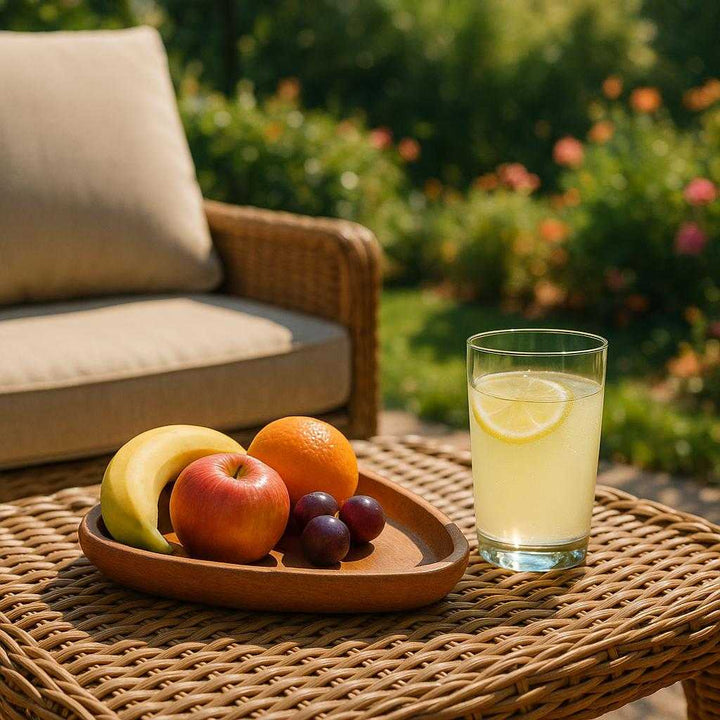 Kaffebakke i valnøddetræ - Moderne og funktionel med naturligt design. A serene outdoor patio setting during a sunny afternoon, where the tray holds an assortment of fruits and a chilled glass of lemonade. It rests on a wicker coffee table next to a comfortable lounge chair. The lush greenery and vibrant flowers in the background create a relaxing vibe, with sunlight highlighting the tray's smooth finish and adding a touch of sophistication to a leisurely afternoon outdoors.