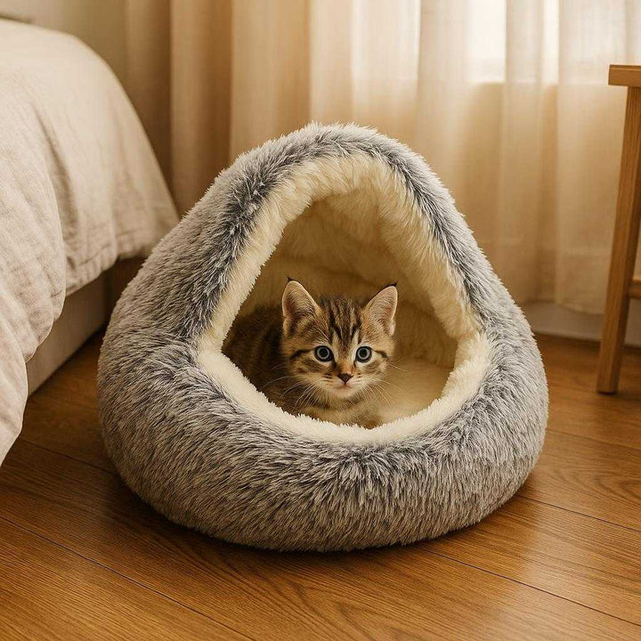 Kattehule i Filt med Hyggelig Kuppelform - Komfort til Store og Små Katte i 40, 50, 60 cm: A different realistic bedroom setting where the cat cave is securely positioned on a wooden floor next to a bed, with a smaller kitten playfully peeking out of the entrance.