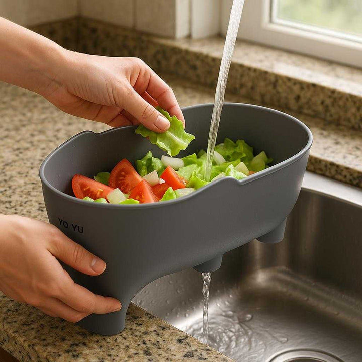 Køkkenredskaber Skyllebeholder til Køkkenvask – Pladsbesparende Grå Afløbsbakke: A realistic kitchen countertop setting where the Kitchen Tools Rinse Holder for Kitchen Sink is properly grounded on a polished granite countertop, being actively used by a person's hands rinsing freshly cut vegetables.