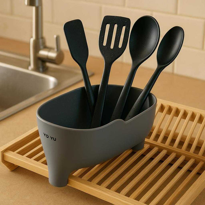 Køkkenredskaber Skyllebeholder til Køkkenvask – Pladsbesparende Grå Afløbsbakke: A different realistic kitchen setting near a sink where the Kitchen Tools Rinse Holder is securely positioned on a wooden dish rack, being used to hold wet utensils like spatulas and spoons after a wash.