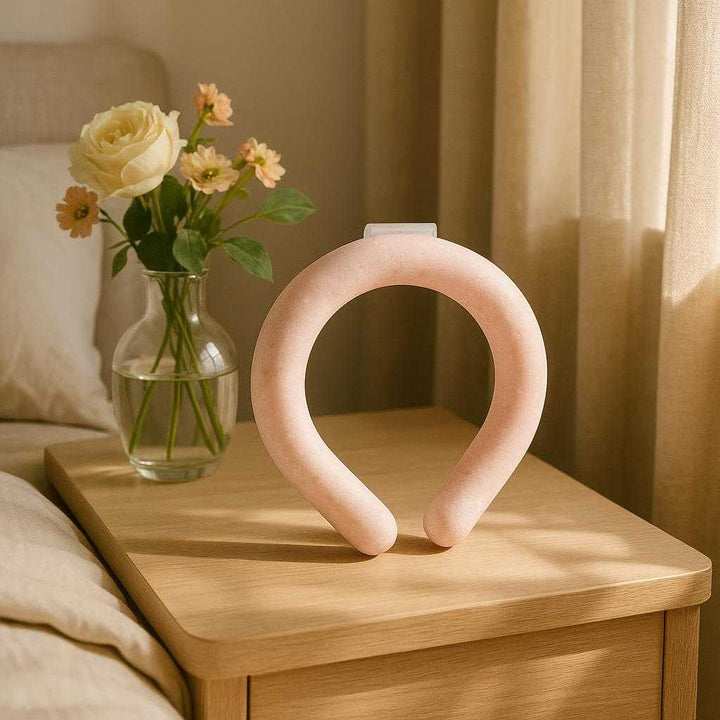 Kølende Omslag til Nakken - Genanvendeligt Gelbånd til Afslapning & Lindring i Lyserød, Blå og Hvid: A different realistic bedroom setting where the Kølende Omslag til Nakken is securely positioned on a bedside table next to a vase of flowers.