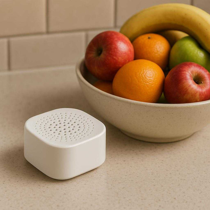 Køleskabsfrisker – Effektiv og Avanceret Lugtneutralisering med Høj Kvalitet. The Køleskabsfrisker sits elegantly on a kitchen counter beside a bowl of colorful fruits, highlighting its minimalistic design and advanced odor-neutralizing capabilities.