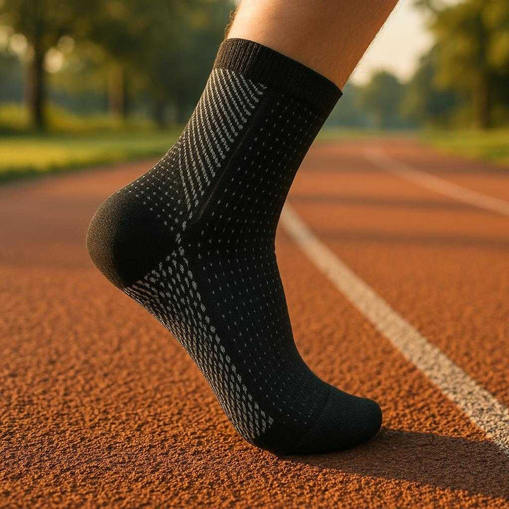 Kompressionsstrømper til løb og hverdagsbrug - Øger blodcirkulation og reducerer hævelse - Tilgængelig i sort og hvid: A realistic outdoor running track setting where the black compression sock is properly grounded on a runner's foot, actively used during a morning jog.