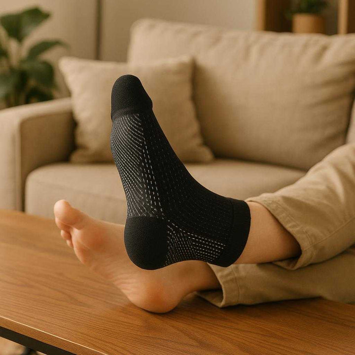 Kompressionsstrømper til løb og hverdagsbrug - Øger blodcirkulation og reducerer hævelse - Tilgængelig i sort og hvid: A cozy living room setting where the black compression sock is securely positioned on a person's foot, naturally placed while they relax on a sofa.