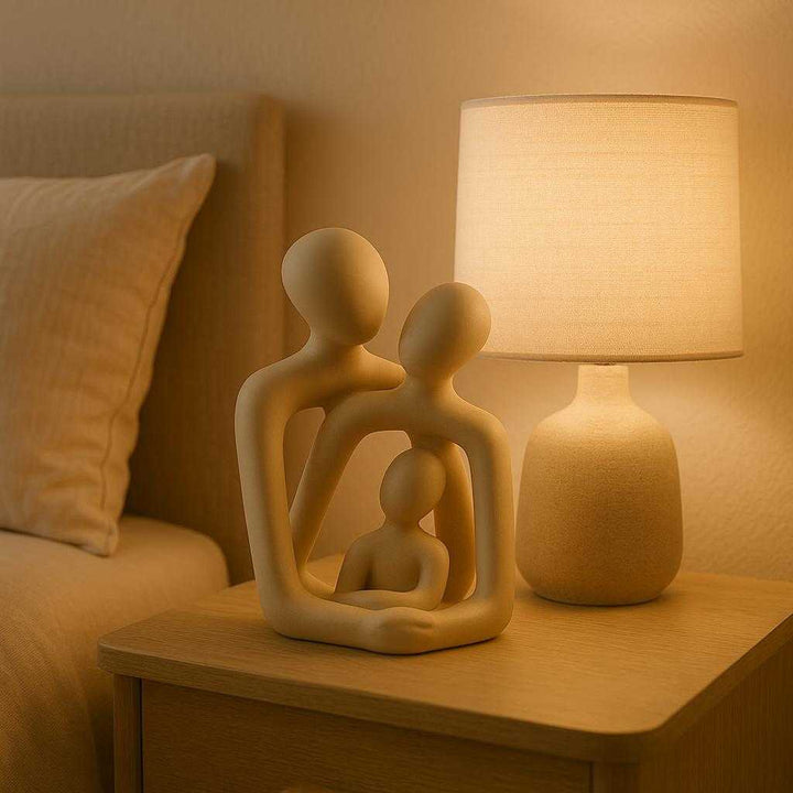 Kærlighedsfigur i Minimalistisk Design - Professionel Abstrakt Skulptur i Keramik, Lys Beige. The abstract ceramic sculpture sits gracefully on a bedside table beside a glowing lamp, casting gentle shadows in a serene bedroom decorated in neutral tones.