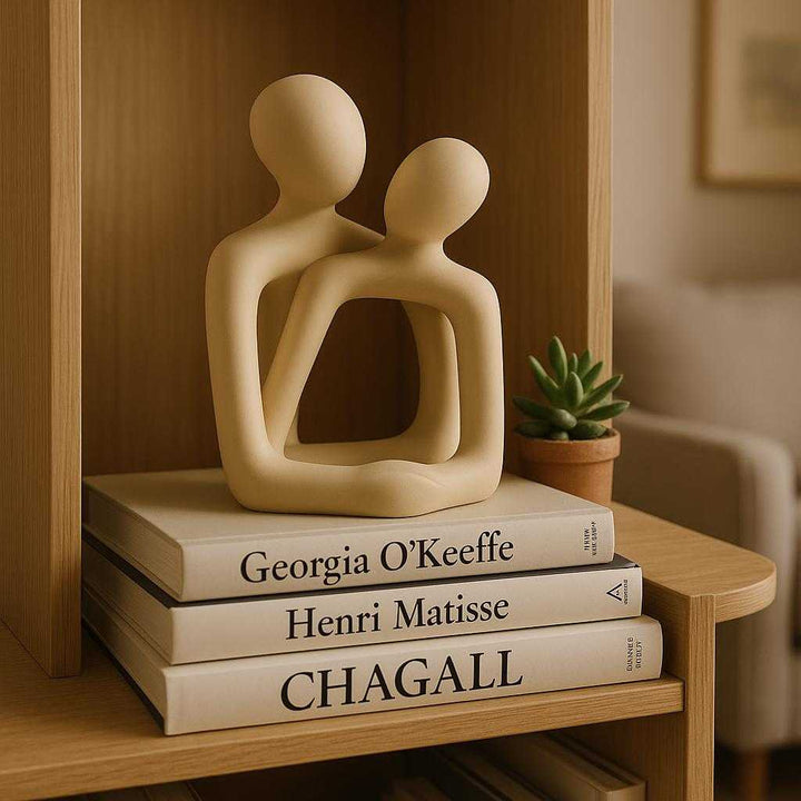 Kærlighedsfigur i Minimalistisk Design - Professionel Abstrakt Skulptur i Keramik, Lys Beige. The ceramic minimalist sculpture is elegantly placed on a modern oak bookshelf, surrounded by art books and a succulent plant, in a cozy living room setting with soft lighting.