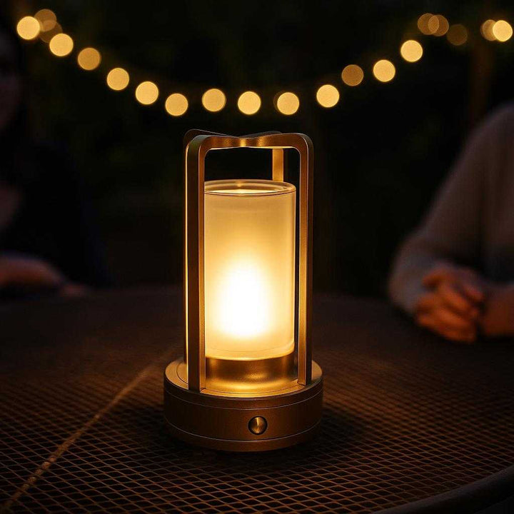 Krystalbordlampe i Retrodesign - Cylinderformet med LED-lys, Batteridrevet, Fås i Guld og Sort: A different realistic outdoor patio setting where the Krystalbordlampe is securely positioned on a metal garden side table, being used during an evening gathering, surrounded by ambient fairy lights and a dimly lit atmosphere, with proper physics, shadows, and realistic integration into the environment, creating a warm and inviting glow.