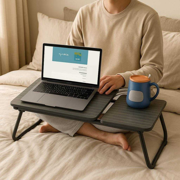 Laptopbord i metal, træ og plastik - Sort, Hvid - Bærbar og Ergonomisk: A realistic bedroom setting where the laptop table is properly grounded on a cozy bed with soft pillows around it, being actively used by a person sitting cross-legged on the bed.
